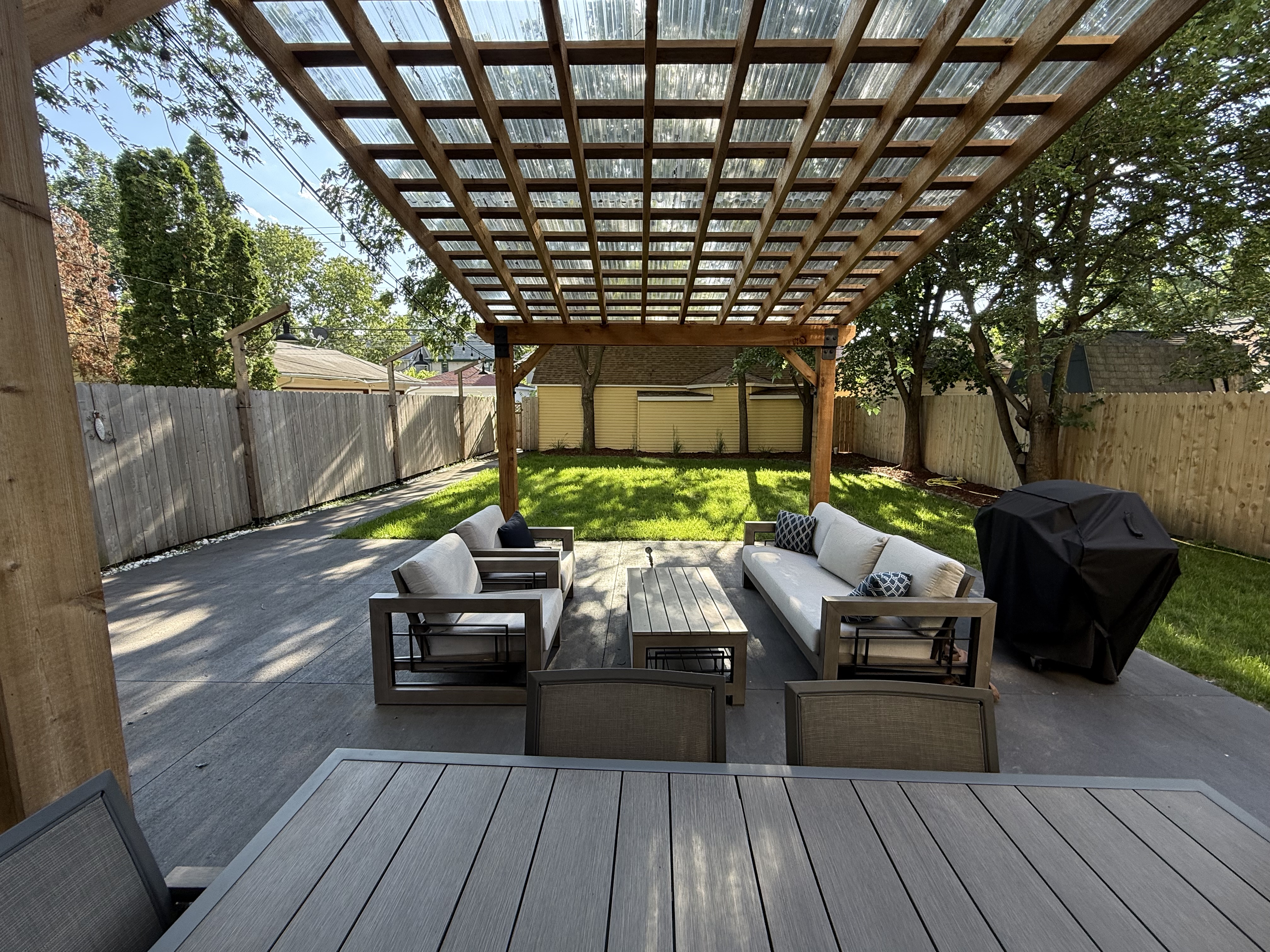 A serene backyard with a cozy pergola seating area and lush green grass.