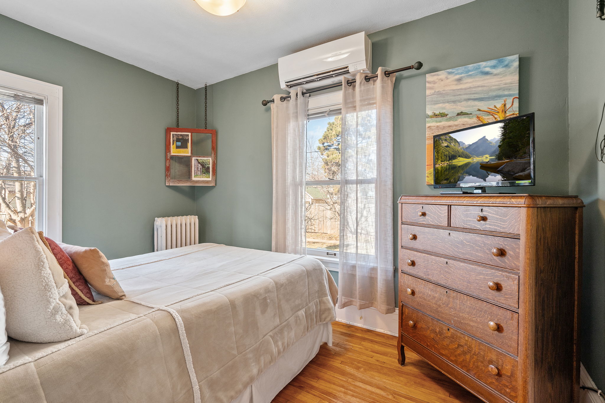 A cozy bedroom featuring a green wall, neatly made bed, and wooden dresser.