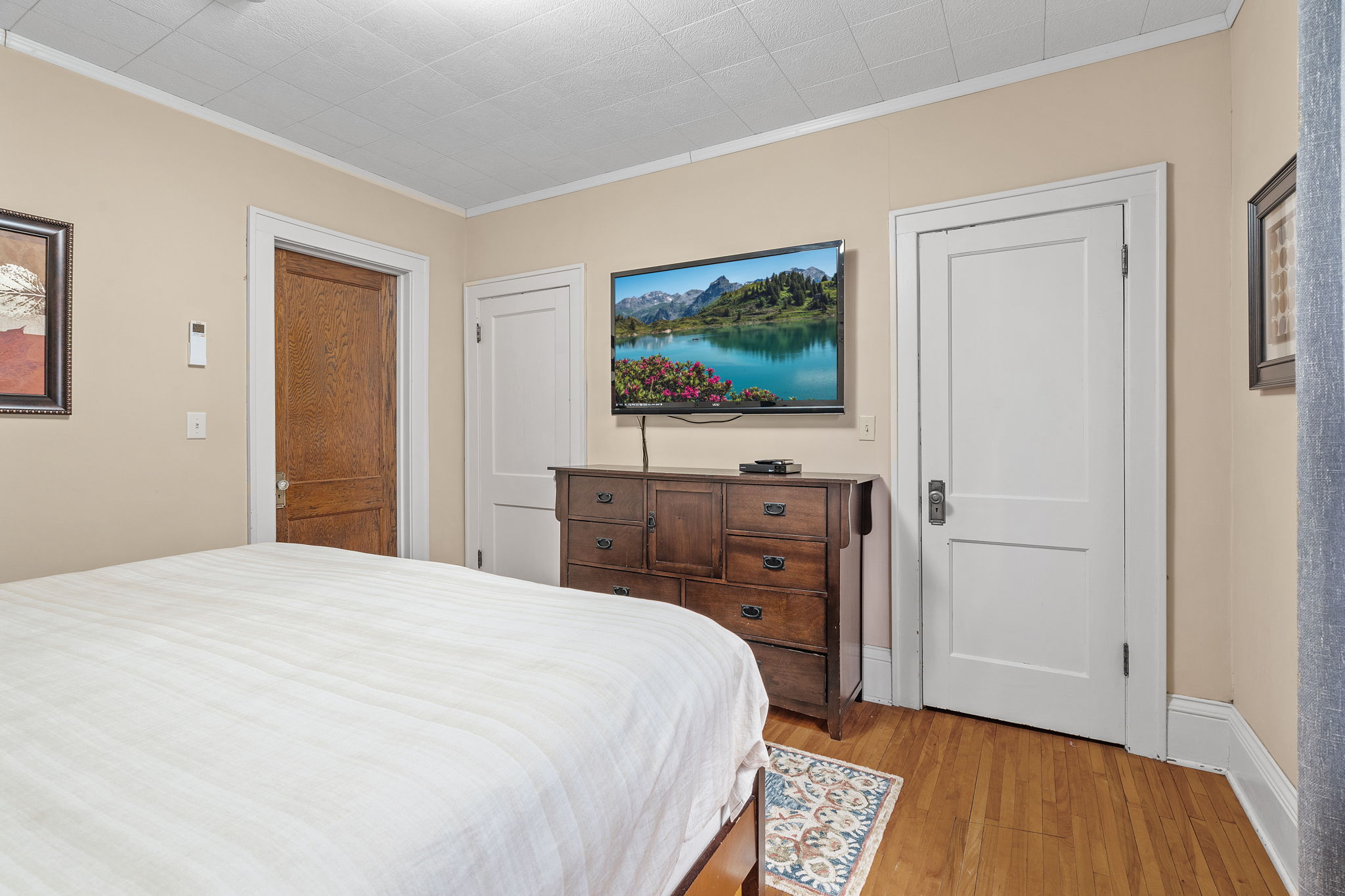 A cozy bedroom with a wooden dresser, a flat-screen TV showing a scenic landscape, and warm-toned decor.