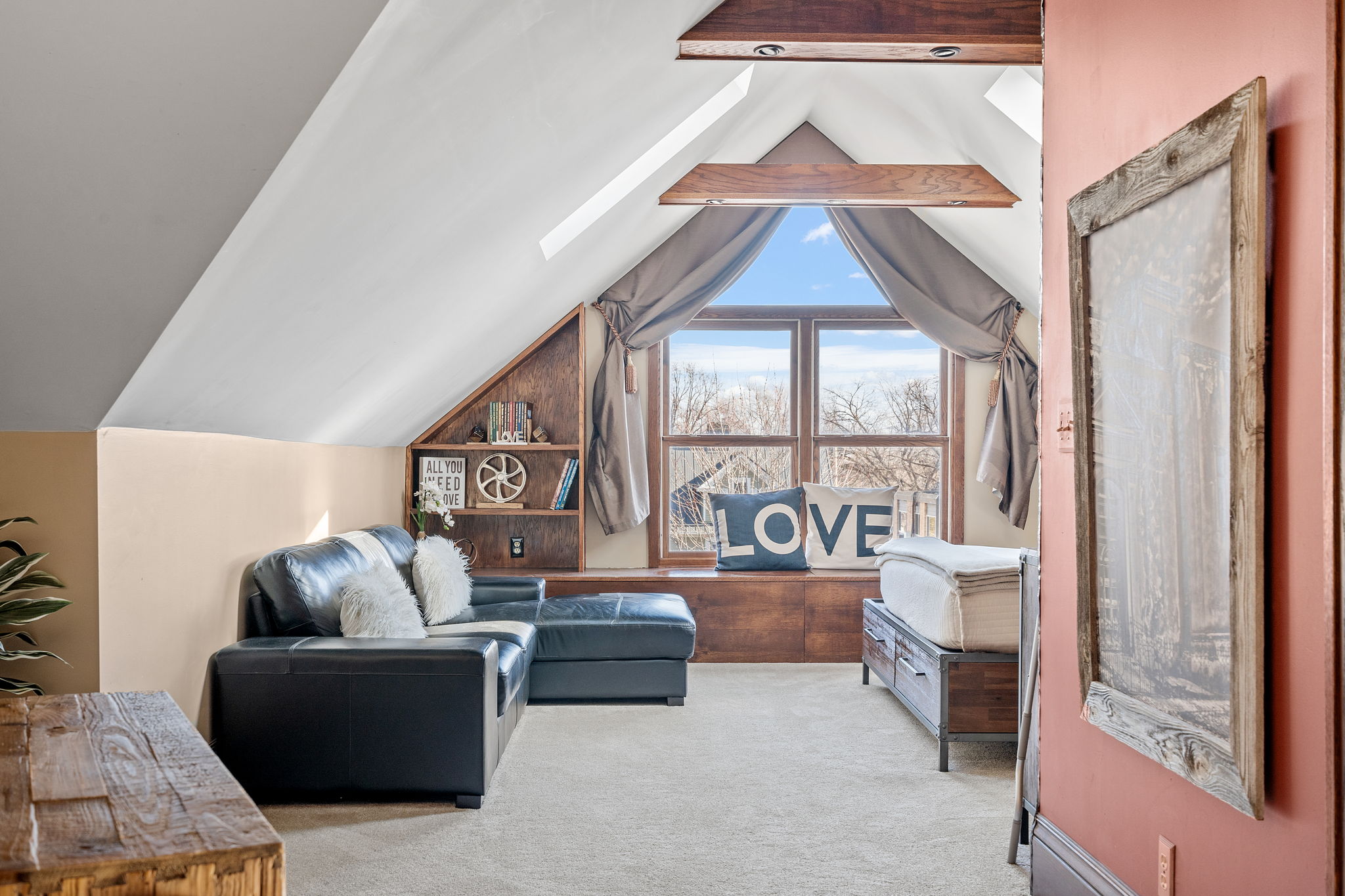 Cozy attic lounge area with a stylish touch, featuring a leather sofa and large windows.