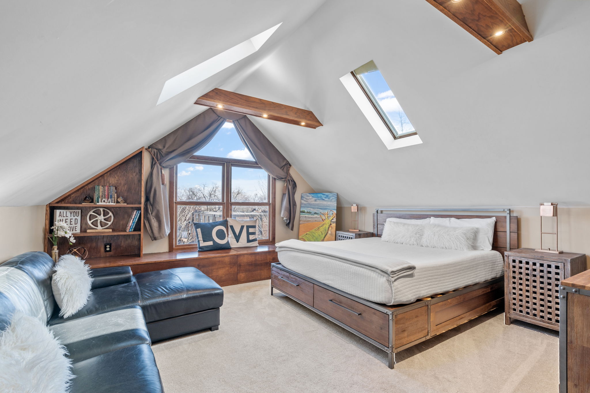 Cozy attic bedroom with a wooden bed, black leather couch, and large window.