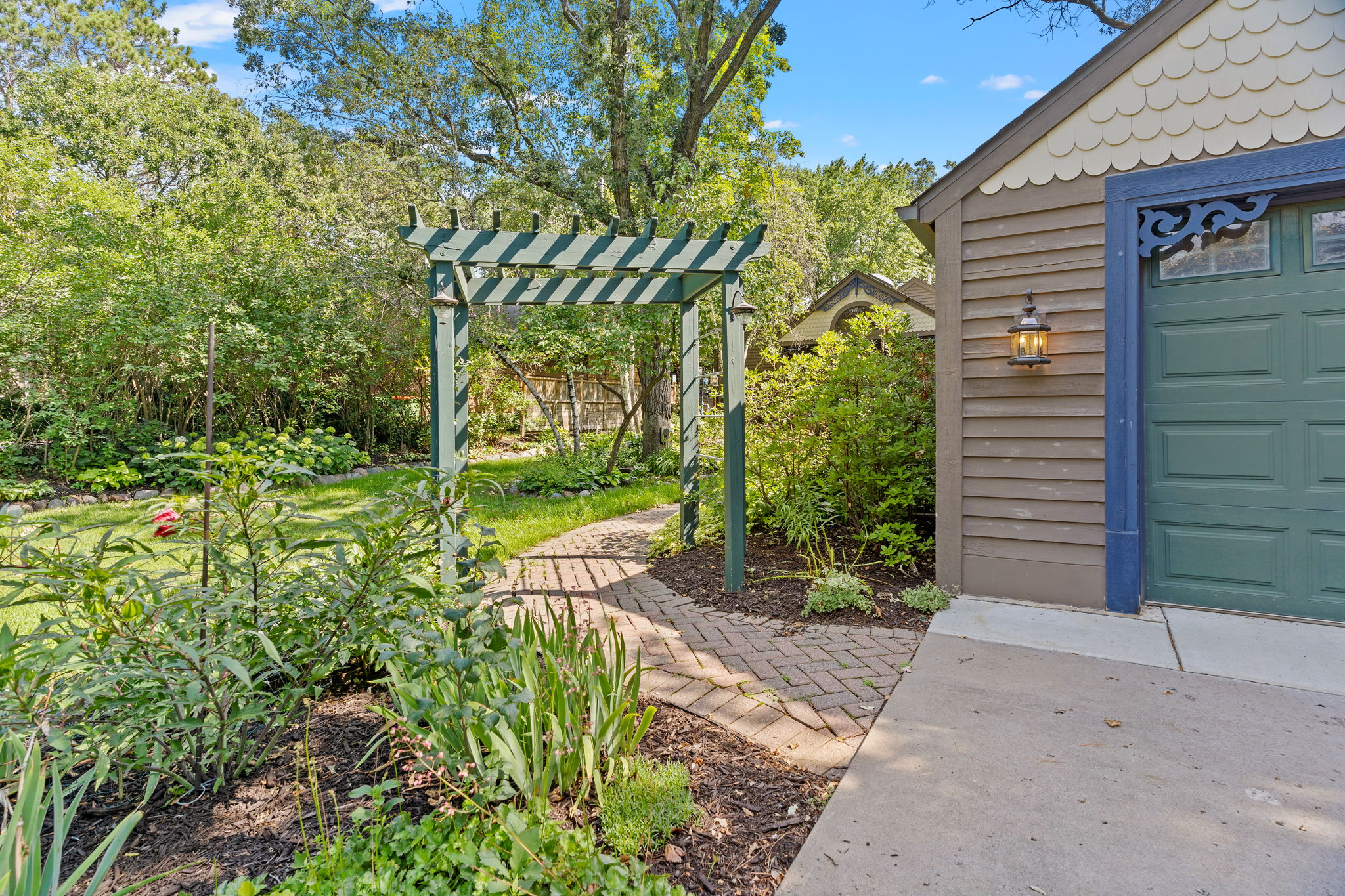 A welcoming garden entrance with a green arbor and winding brick path leading to a home.