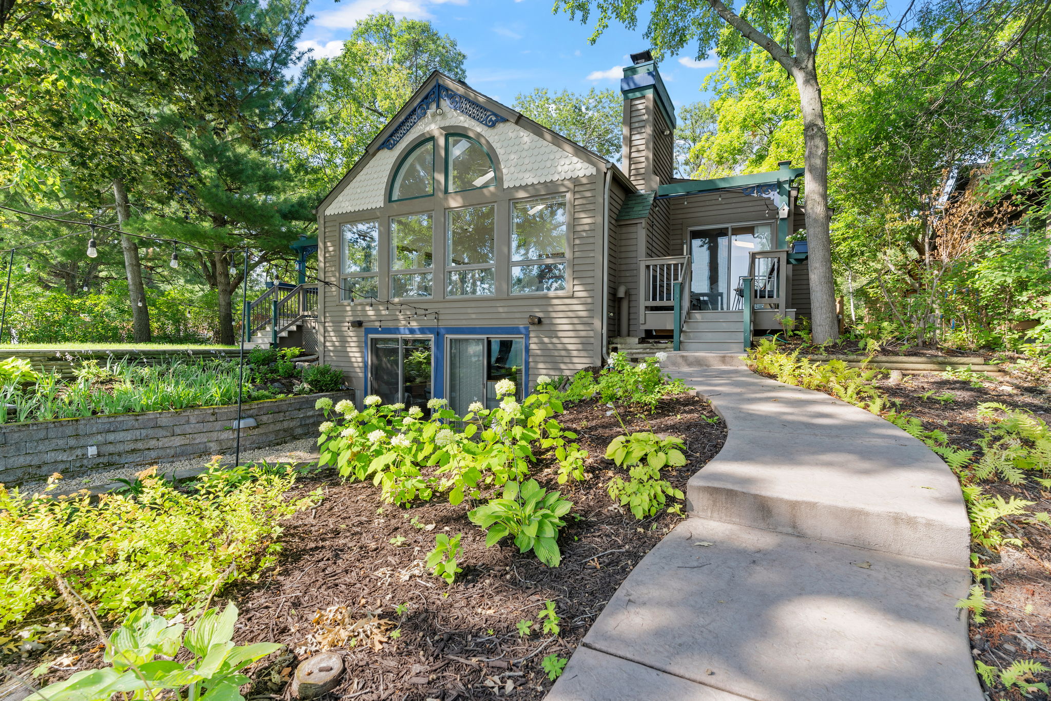 A charming modern house surrounded by lush greenery, featuring a welcoming pathway and large windows.