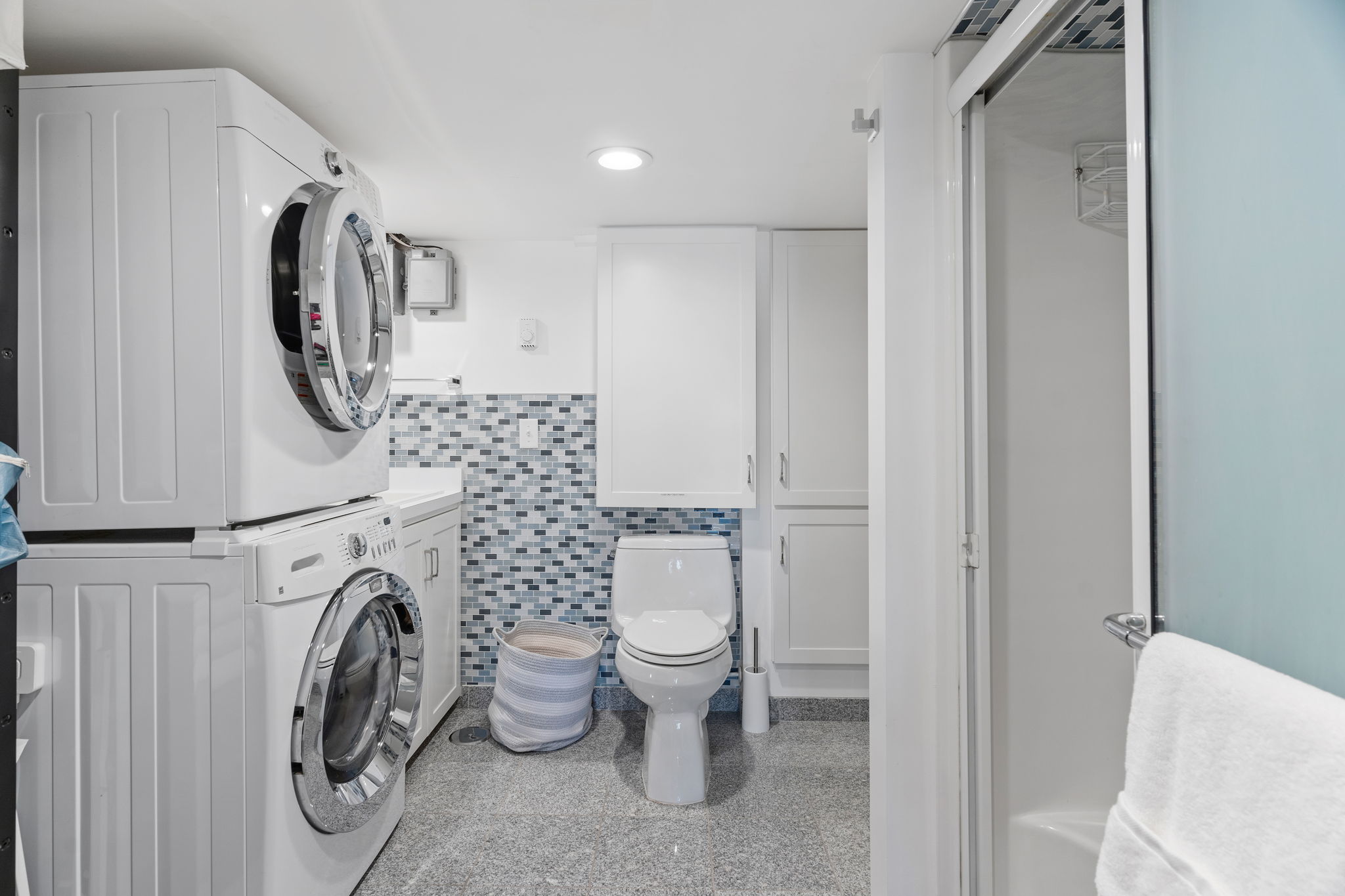 A modern laundry and bathroom space featuring a stacked washer and dryer, stylish mosaic backsplash, and sleek fixtures.
