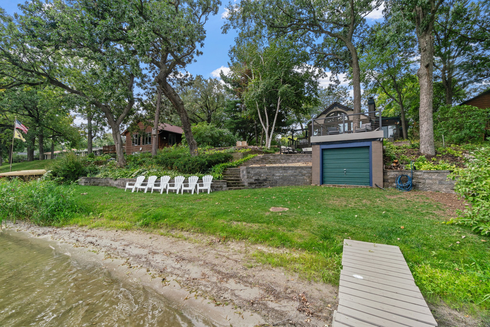 A tranquil lakeside scene with white chairs and a charming house in the background.