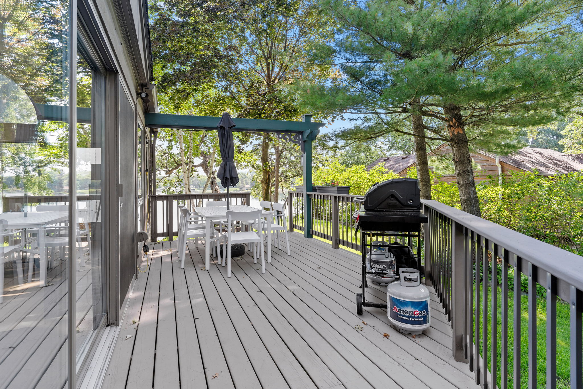 A tranquil outdoor deck featuring a dining area and a grill, surrounded by lush trees.