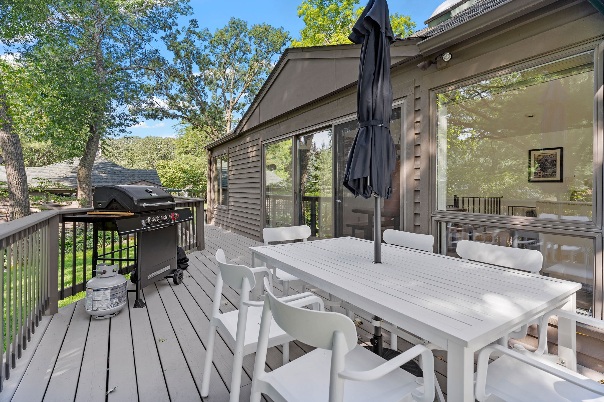 A modern outdoor deck featuring a grill and dining area surrounded by lush trees.