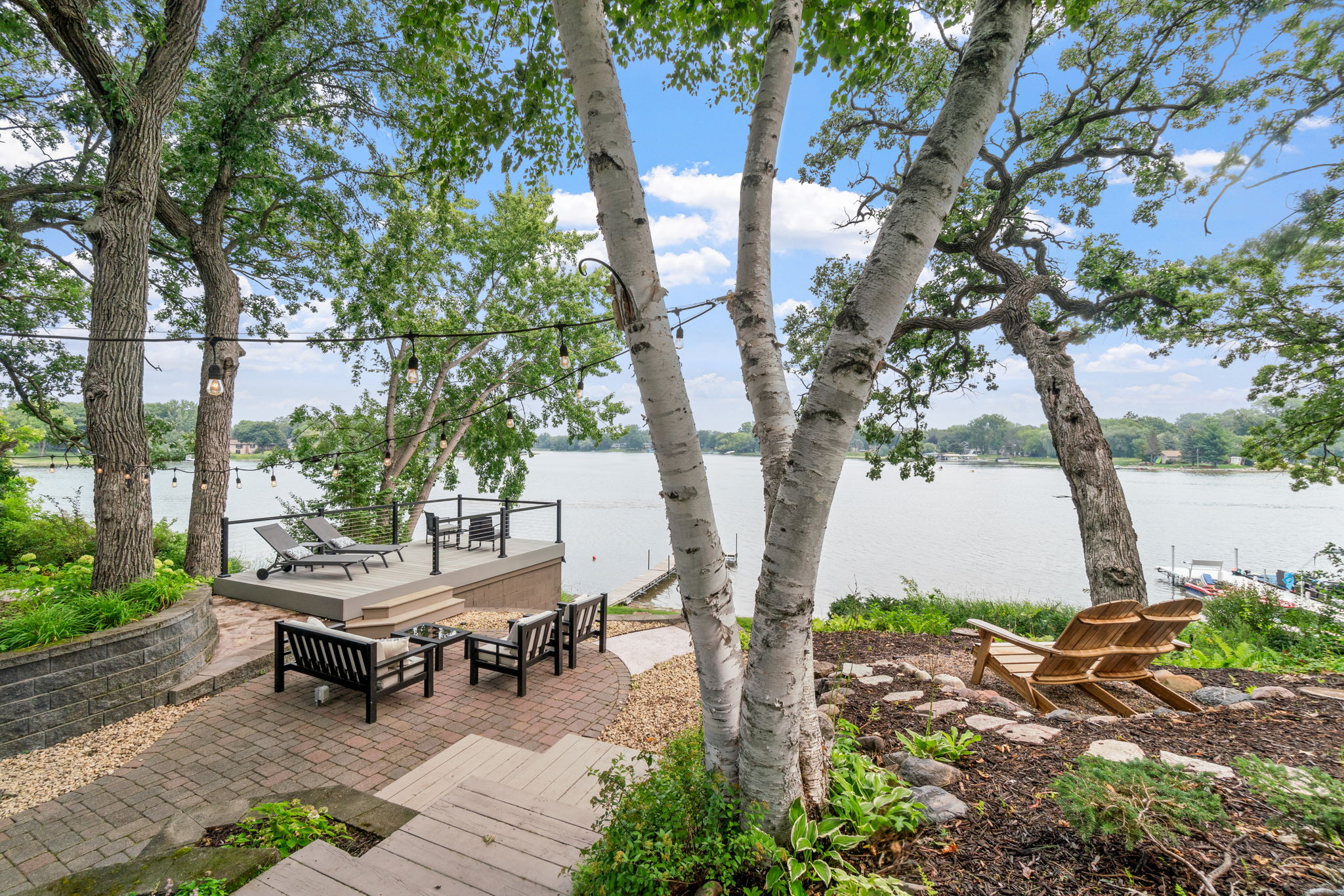 A picturesque lakeside retreat featuring cozy seating and sun lounges under lush trees.