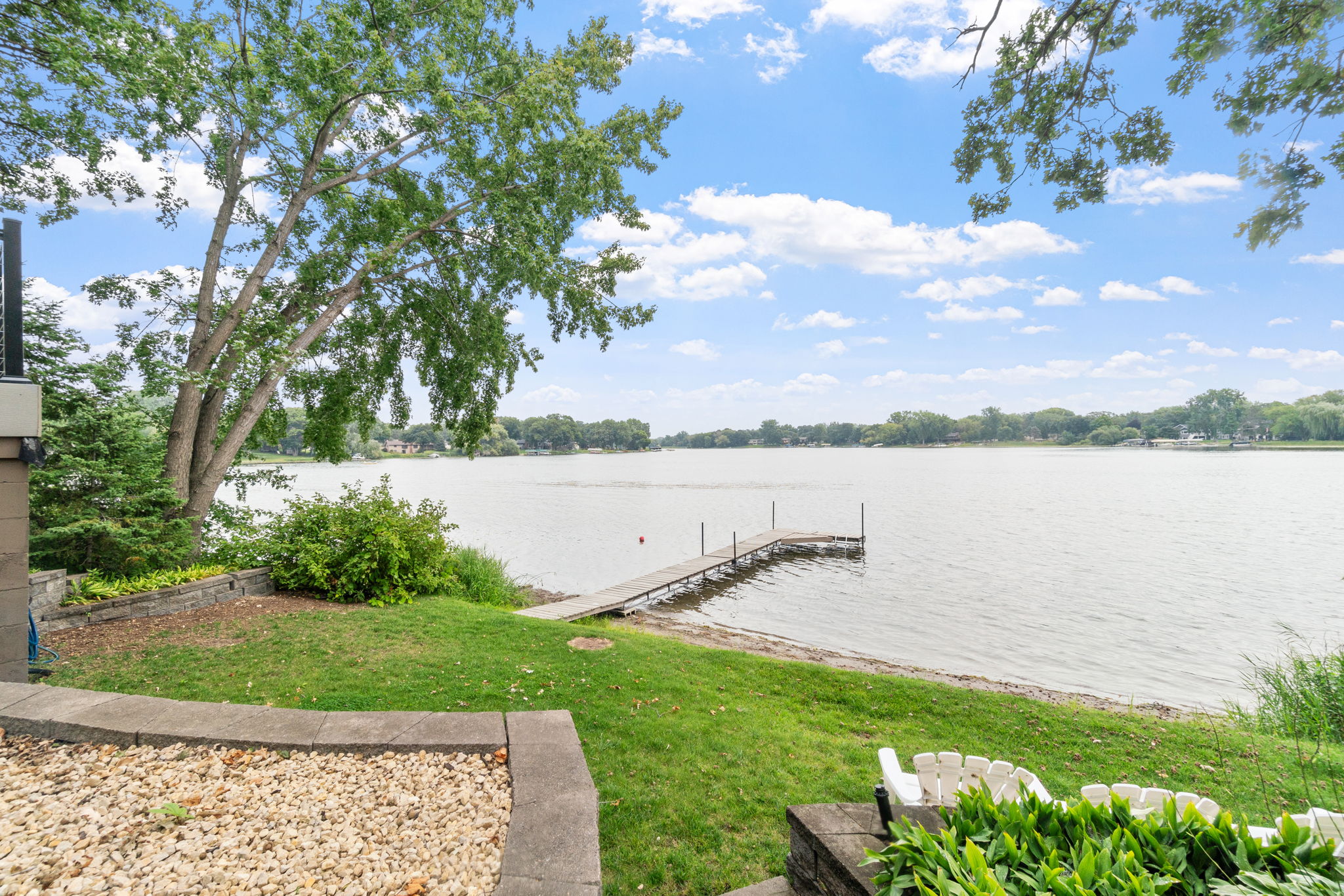 A peaceful lakeside view with a wooden dock under a blue sky.