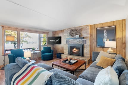 A cozy living room with teal furniture, a brick fireplace, and large windows showing a lake view.