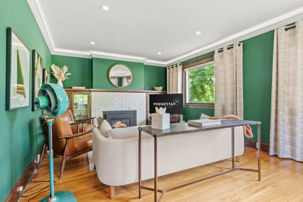 A modern living room with green walls, beige sofa, turquoise fan, and a white brick fireplace.