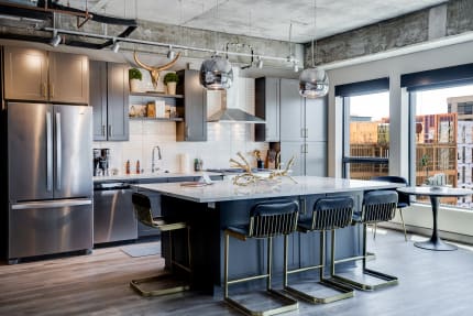 Modern kitchen featuring dark cabinetry, white countertops, and stylish bar stools, illuminated by pendant lights.