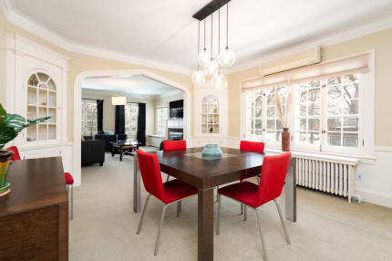 Modern dining room with a wooden table, red chairs, and an open archway leading to a living area.