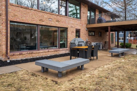Outdoor patio area with a dining table, chairs, and a grill adjacent to a brick house.