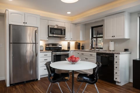 A modern kitchen with white cabinets, stainless steel appliances, and a round table with a bowl of red apples.