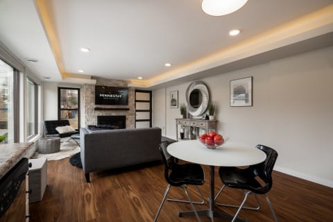 Cozy modern living room with a dining area, featuring a gray sofa, stone fireplace, and round dining table with black chairs.
