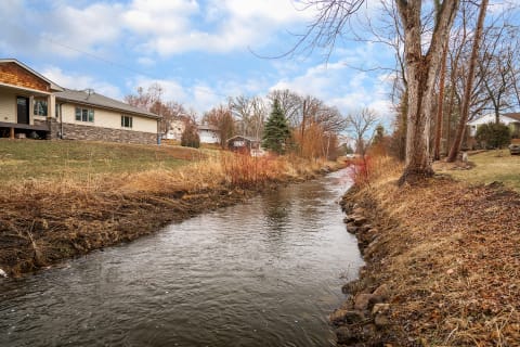 A calm stream flows through a suburban area, with homes and trees in the background.