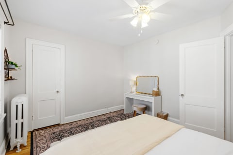 A bright bedroom featuring a bed, dressing table with a mirror, and vintage radiator.
