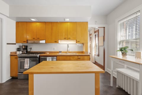 A modern kitchen featuring warm wood cabinetry, stainless steel appliances, and a small wooden island.