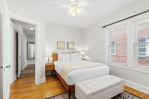 A cozy bedroom with a bed, wooden furniture, and natural light from windows.