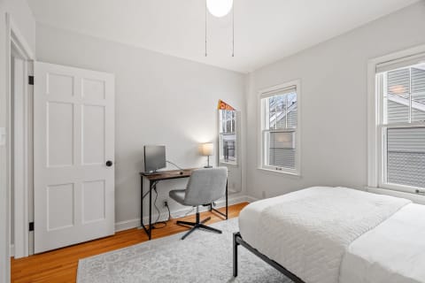 A bright bedroom with a bed, desk, and window overlooking the outdoors.