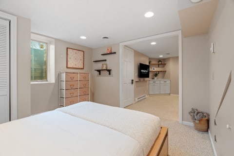 A bright basement bedroom with a bed, window, and storage drawers.