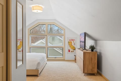 Cozy attic bedroom with a sloped ceiling and large bay window.