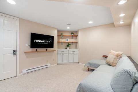 A nicely decorated basement living area featuring a television, a couch, and shelves with decor.