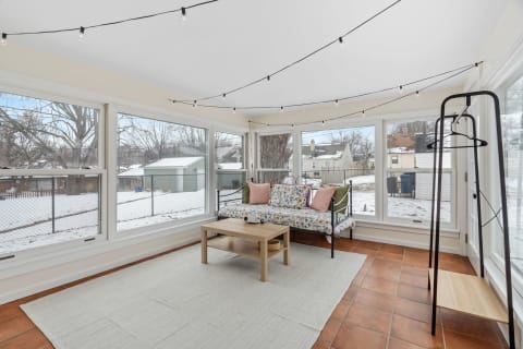 Sunroom with large windows, a floral daybed, decorative lights, and snow outside.