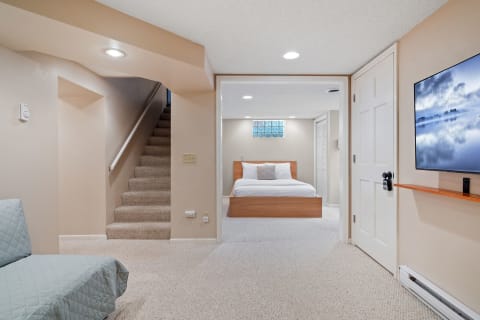 A well-designed basement living area featuring a couch, a staircase, and a bedroom with a bed and television.
