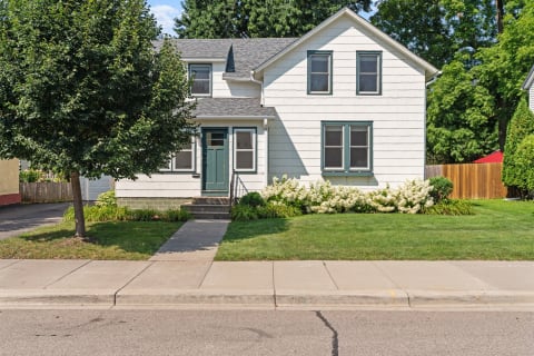 A two-story house with white siding, green trim, and a front lawn adorned with flowers.