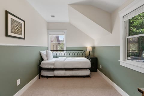 A cozy bedroom with a twin bed, green walls, and a window showing greenery outside.