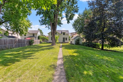 Backyard view with a path, trees, and a residential house.