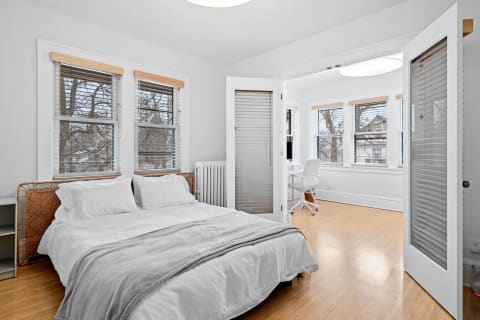 A cozy bedroom featuring a woven headboard bed, large windows, and a study area.