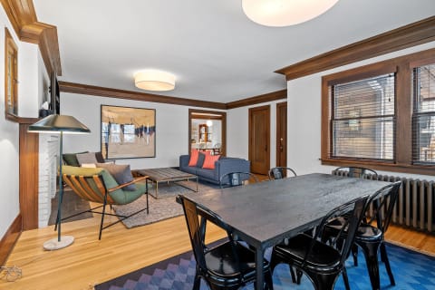 Living room with a green armchair, navy blue couch, and black dining table, featuring wooden accents and an abstract painting.