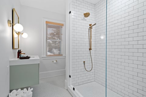 Modern bathroom featuring a glass-enclosed shower, golden fixtures, and a soft green sink cabinet.