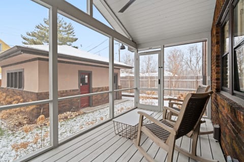 Screened-in porch with wooden rocking chairs, a table, and a view of the snowy yard.