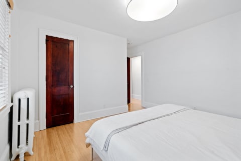 Minimalistic bedroom with white walls, light wood flooring, and a wooden door.