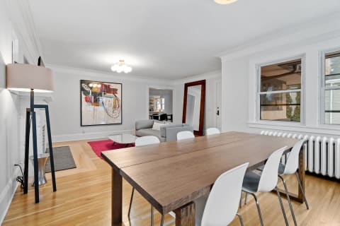 Spacious dining area featuring a wooden table, white chairs, abstract artwork, and a gray sofa in the living room.