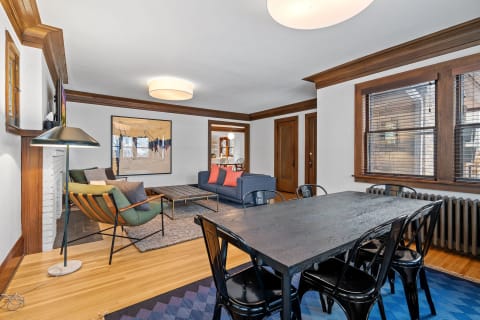 A stylish living space featuring a green armchair, navy sofa with colorful pillows, and a dining table with black chairs.