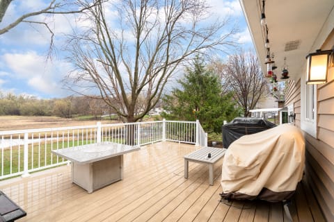 A spacious outdoor deck with a table and grill cover, surrounded by trees and a stream.