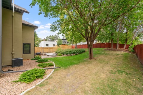 A view of a backyard with a modern house, lawn, shrubs, and outdoor seating.