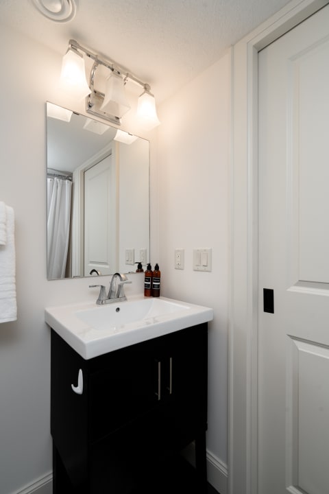 A modern bathroom featuring a white countertop sink on a dark vanity, illuminated by stylish light fixtures.