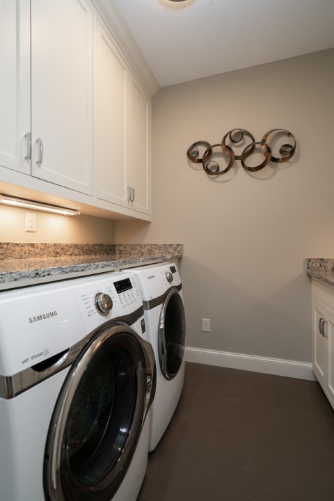 Well-designed laundry room with Samsung washing machines and a decorative metal wall art.