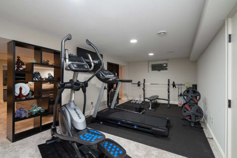 Home gym featuring an elliptical machine, treadmill, weight bench, and decorative shelving.