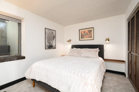 Cozy bedroom with a king-sized bed, decorative pillows, framed art, and natural light from a window.