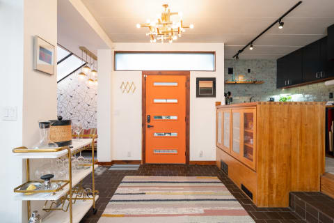 Entryway with an orange door, geometric wall design, and modern bar cart.