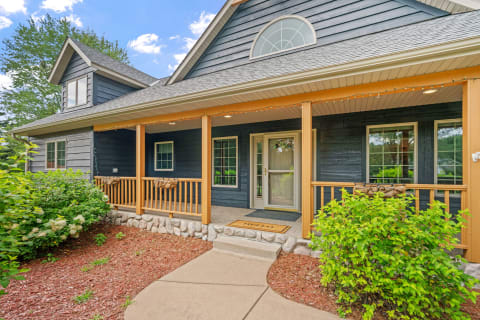 A front view of a blue house with a porch and lush plants.