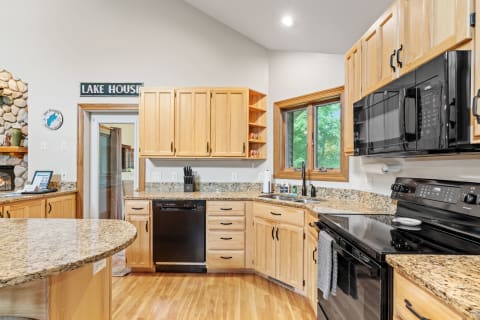 Modern kitchen with wood cabinets, granite countertops, and a window overlooking green trees.