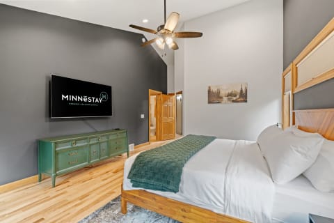 Stylish bedroom with a king-sized bed, green throw blanket, mounted TV, and wooden dresser.